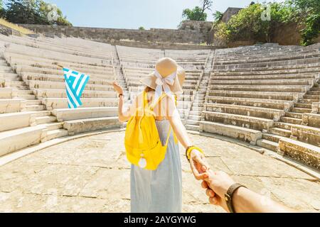 Ragazza asiatica turistica che viaggia nelle rovine di un'antica Acropoli o l'anfiteatro con una bandiera greca. Concetto attivo di giovani viaggiatori e studenti Foto Stock