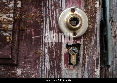 Parte di una vecchia porta marrone con una maniglia rotta e una serratura della porta. La vernice sulla porta è sbiadita e sbriciolata. Foto di primo piano della parte anteriore Foto Stock