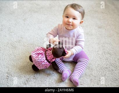 La ragazza felice del bambino gioca con l'orso del giocattolo sul pavimento a casa Foto Stock