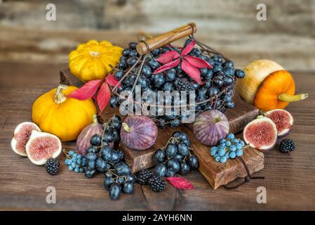 Bell'autunno ancora vita: Uva nera in un cesto sul vecchio tagliere così come fichi maturi, lamponi rossi, zucca arancione e more Foto Stock