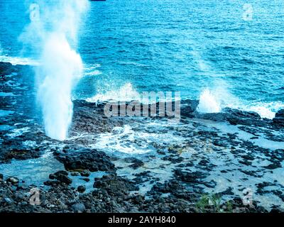 Blolole di lava nelle Hawaii. L'oceano erode la piattaforma di lava sott'acqua e poi soffia attraverso i fori nella parte superiore. Foto Stock