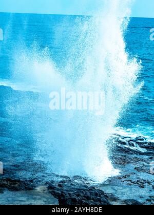 Blolole di lava nelle Hawaii. L'oceano erode la piattaforma di lava sott'acqua e poi soffia attraverso i fori nella parte superiore. Foto Stock