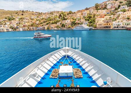 La prua della nave da crociera che domina l'attrazione turistica - la città e l'isola di Symi, Grecia Foto Stock