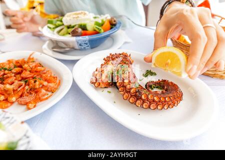 Primo piano di una donna che mangia deliziosi frutti di mare - gamberi e polpo alla griglia e insalata di verdure. Il concetto di cucina mediterranea e di cibo sano Foto Stock