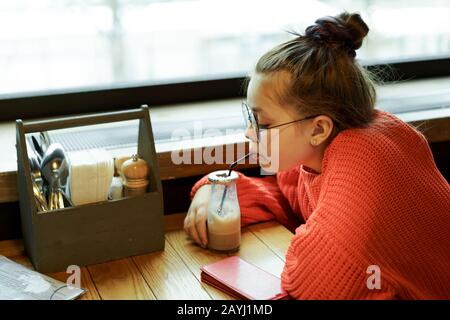 Ragazza adolescente seduto in un caffè a un tavolo in attesa e bere Foto Stock