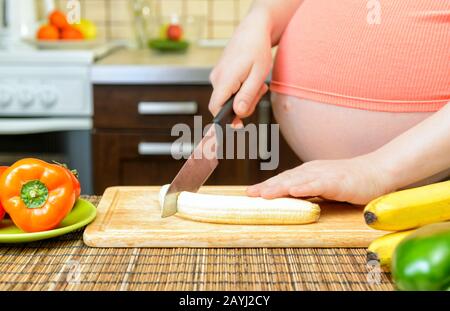 Donna incinta prepara una banana in cucina. Cibo sano. Foto Stock