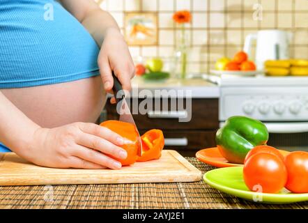 Donna incinta che prepara cibo vegetale in cucina Foto Stock