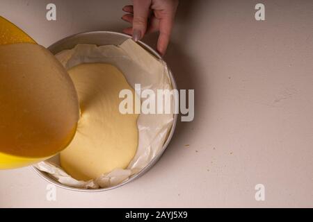 Donna che versa l'impasto per una torta in uno stampo di alluminio imbottito con carta pergamena. Foto Stock