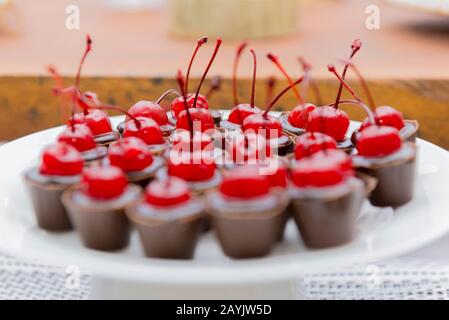 Piatto bianco con molte tazze di cioccolato ricoperte di ciliegia. Festa di compleanno caramella closeup. Messa a fuoco selettiva. Deliziosa caramella da festa, dolci da festa, re Foto Stock