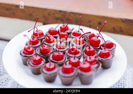 Piatto bianco con molte tazze di cioccolato ricoperte di ciliegia. Festa di compleanno caramella closeup. Messa a fuoco selettiva. Deliziosa caramella da festa, dolci da festa, re Foto Stock