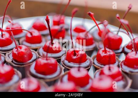 Piatto bianco con molte tazze di cioccolato ricoperte di ciliegia. Festa di compleanno caramella closeup. Messa a fuoco selettiva. Deliziosa caramella da festa, dolci da festa, re Foto Stock