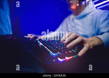 Streamer giovane uomo gioisce nella vittoria giocatore professionista che gioca a giochi online computer con cuffie, colore neon Foto Stock