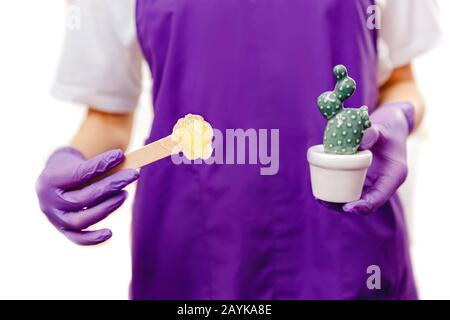 Mani ravvicinate di un maestro di bellezza nei guanti tiene la spatola con pasta per la depilazione dello zucchero e cactus. Capelli lisci che tirano il concetto Foto Stock