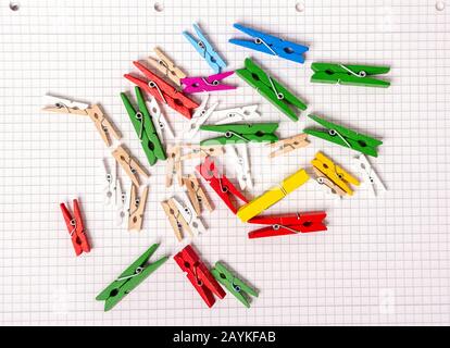 I clothespins di legno di colori differenti e le misure differenti giacciono su un foglio del notepad. Colori brillanti. Foto Stock