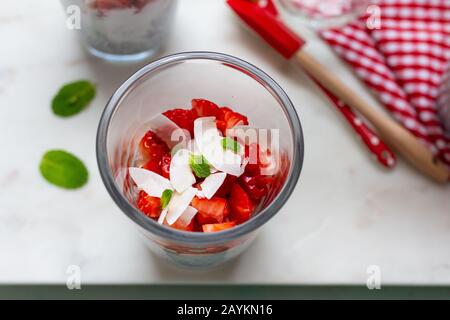 Vista in primo piano della parte superiore di un bicchiere pieno di fragole. Alcune foglie di menta sono sulla parte superiore oltre ad alcuni chip di cocco. Foto Stock