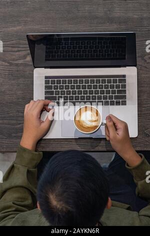 Uomo che beve caffè caldo e che usa un computer portatile Foto Stock