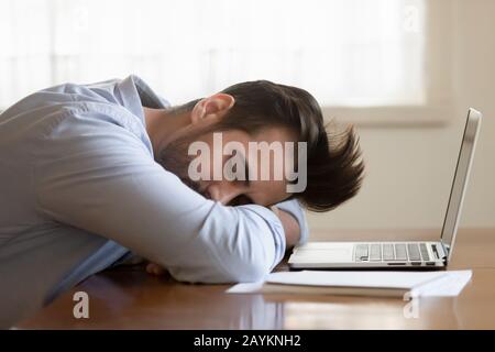 Lavoratore maschile esausto addormentarsi sul posto di lavoro Foto Stock