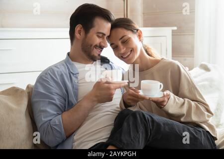 Amorevole giovane coppia abbraccio sul divano bere tè Foto Stock