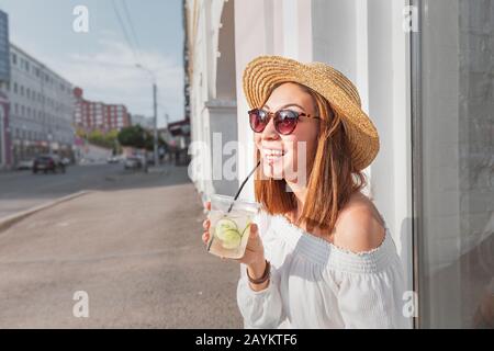 Primo piano di donna asiatica bevendo bevande detox con cetrioli e limonata all'aperto nella strada della città Foto Stock