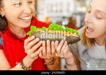 Amici multirazziali allegri mangiare sandwich e divertirsi in una caffetteria Foto Stock