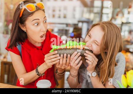 Amici multirazziali allegri mangiare sandwich e divertirsi in una caffetteria Foto Stock