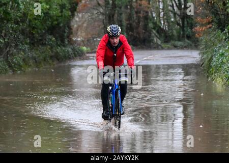 Sidmouth, Devon, Regno Unito. 16th febbraio 2020. Meteo Regno Unito. Un ciclista corre attraverso l'acqua alluvionale da pioggia pesante da Storm Dennis sulla B3176 vicino a Sidmouth nel Devon. Foto Di Credito: Graham Hunt/Alamy Live News Foto Stock