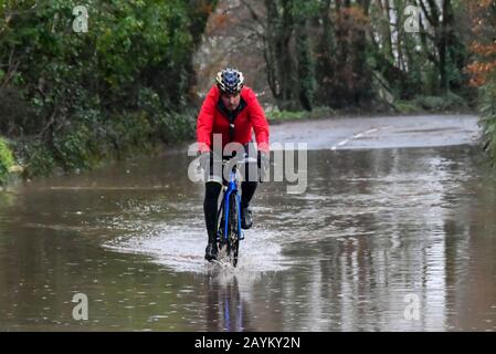 Sidmouth, Devon, Regno Unito. 16th febbraio 2020. Meteo Regno Unito. Un ciclista corre attraverso l'acqua alluvionale da pioggia pesante da Storm Dennis sulla B3176 vicino a Sidmouth nel Devon. Foto Di Credito: Graham Hunt/Alamy Live News Foto Stock