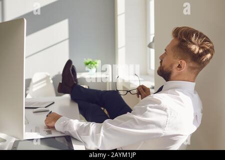 L'uomo d'affari riposa meditando i sogni sul posto di lavoro al tavolo con un computer in ufficio Foto Stock