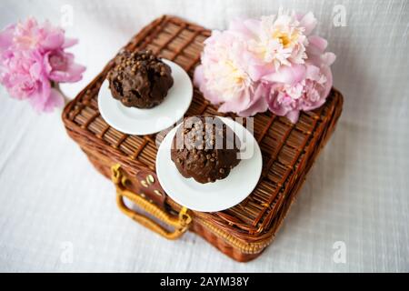 Muffin al cioccolato e di un bel colore rosa peonie giacciono su una valigia di legno. Bella composizione. Foto Stock