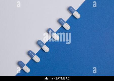 Fila di pillole disposte su sfondo blu e bianco. Sfondo farmaci farmaceutici. Foto Stock