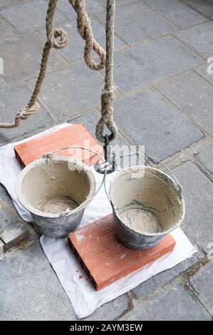 Due secchi in cemento vuoti appesi pronti per essere riempiti e tirati su una puleggia a fune in un cantiere esterno Foto Stock