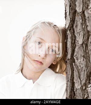 Una giovane ragazza bionda introspettiva dai capelli biondi, con occhi blu e un aspetto triste sul suo viso, indossando una camicia bianca. Foto Stock