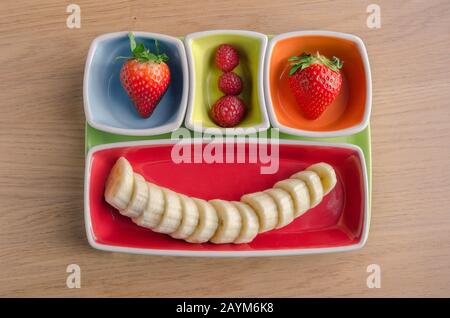 Fragole, lamponi e banane sono stati utilizzati per creare un emoticon. Dessert di frutta in piatti carini Foto Stock