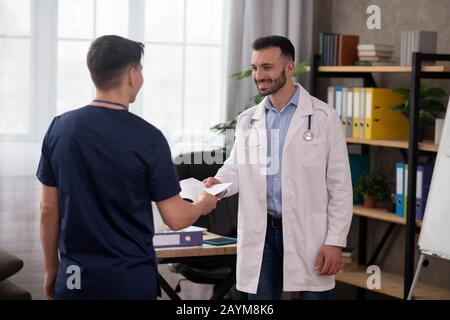 Bearded il medico della testa che scuote le mani con l'intern giovane Foto Stock