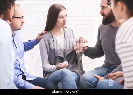 Membri del gruppo di terapia confortante donna sconvolta all'incontro della comunità in riabilitazione Foto Stock