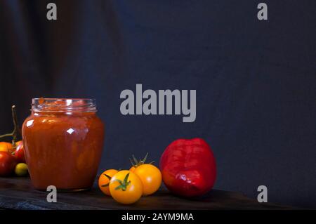 ketchup rosso fatto in casa in una composizione con pomodori maturi Foto Stock