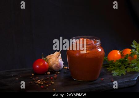 ketchup rosso fatto in casa in una composizione con pomodori maturi Foto Stock