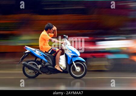 Motociclista che protegge gli occhi con la mano contro la pioggia, Thailandia, Phuket Foto Stock