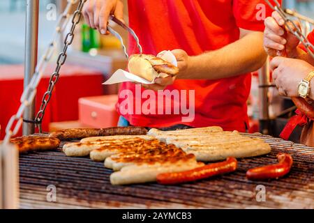 Uomo che cucina le salsicce su un grill piatto al mercato alimentare Street Foto Stock