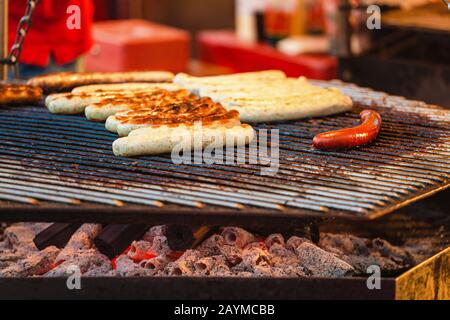 Uomo che cucina le salsicce su un grill piatto al mercato alimentare Street Foto Stock