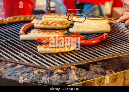Uomo che cucina le salsicce su un grill piatto al mercato alimentare Street Foto Stock