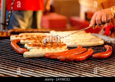 Uomo che cucina le salsicce su un grill piatto al mercato alimentare Street Foto Stock