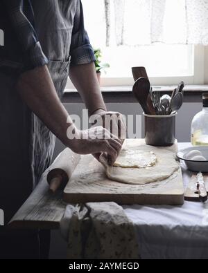 Gli uomini coltivano le mani che cucinano il cibo, rotola fuori l'impasto su un tavolo in una cucina di stile provenzale Foto Stock