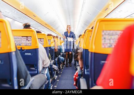 16 MAGGIO 2018, BUDAPEST UNGHERIA: Interno dell'aereo Ryaniar con passeggeri su sedili e stewardess in uniforme a piedi la corsia Foto Stock