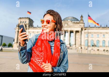 Bella giovane donna in abbigliamento casual che comunica con il suo cellulare internet al Bundestag, Berlino Foto Stock