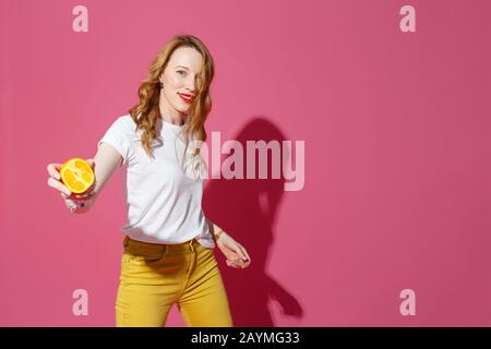 Frutti d'arancia, mangiare sano, vere emozioni - una giovane donna bionda che giocolce arance su sfondo rosa - dieta, persone e concetto di umore. Foto Stock