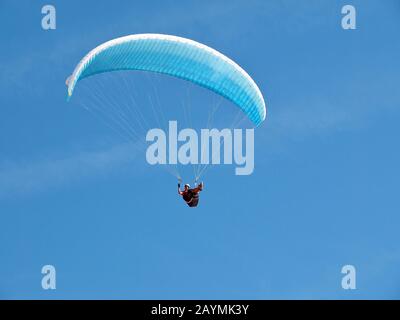 Un uomo vola nel suo parapendio davanti al cielo blu Foto Stock