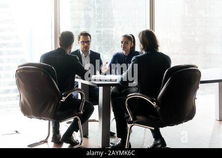Un uomo d'affari fiducioso con un collega che ha acceso la discussione con i partner seduti. Foto Stock