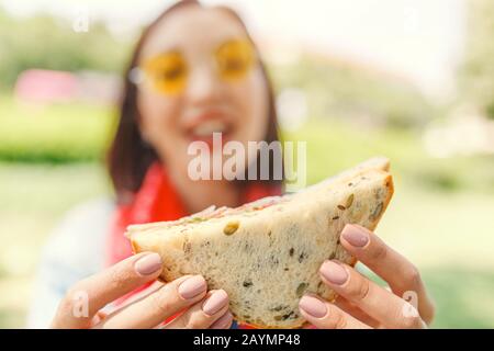 Giovane donna mangiare sandwich e fare una pausa pranzo all'aperto nel parco Foto Stock