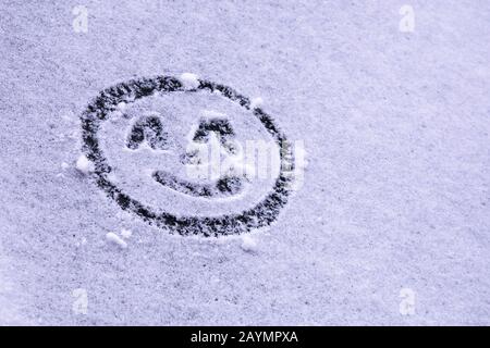 Sorridente emoticon felice disegnato sulla neve sul parabrezza. Accoglienza e celebrazione delle attese lunghe prima neve e arrivo invernale Foto Stock